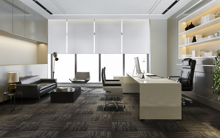 Modern office with white desk, black sofa, shelving, and large windows letting in soft daylight