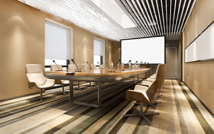 Modern conference room with long wooden table, beige chairs, wall screen, and striped ceiling lighting