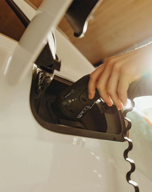 Hand plugging a charging cable into a white electric car’s charging port
