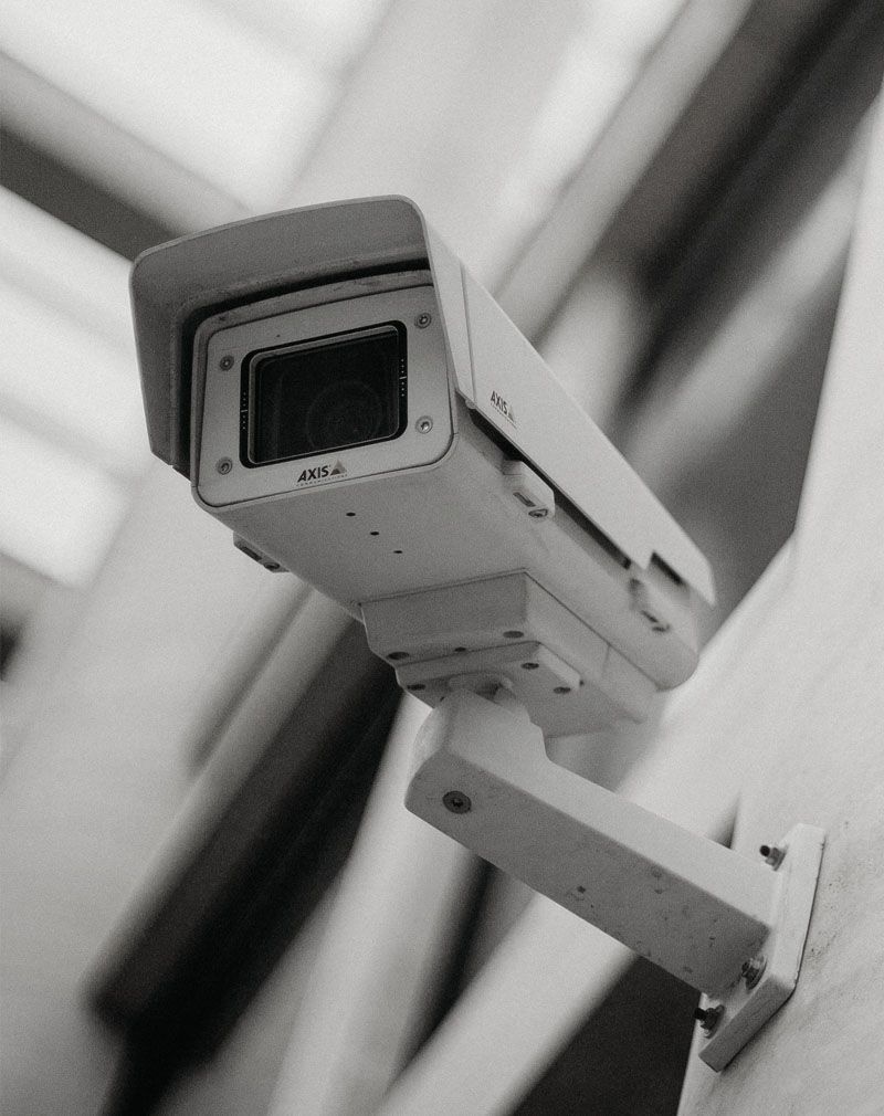 Black-and-white security camera mounted on a wall, angled upward in an indoor setting