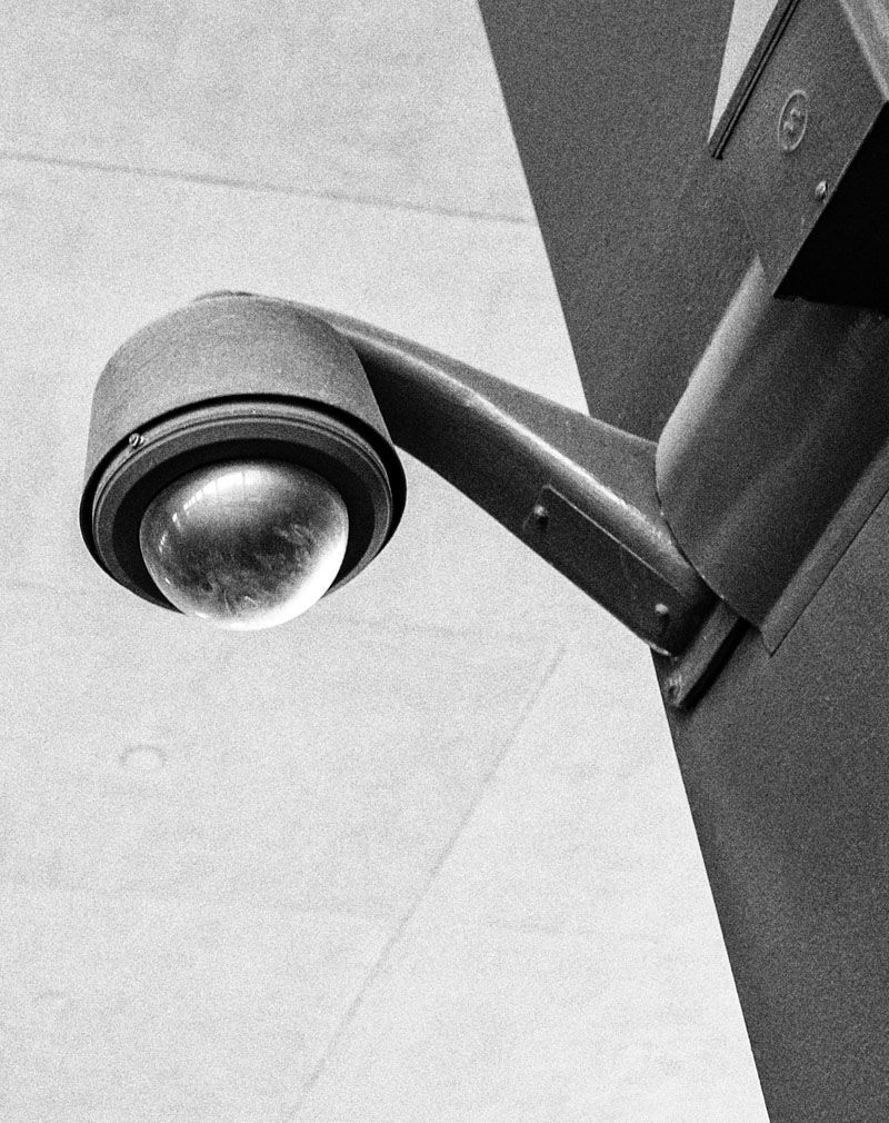 Black-and-white security camera mounted on a wall, angled downward.