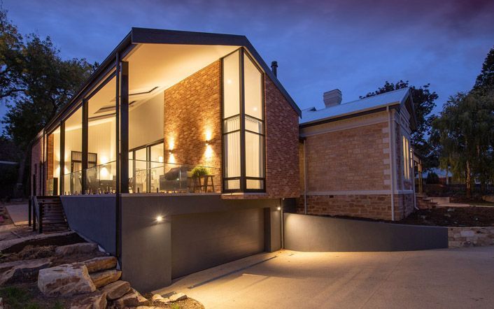 Modern house exterior at dusk with large glass windows and warm interior lighting