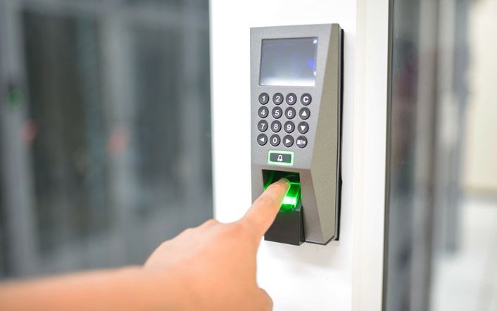 Finger pressing a glowing green access keypad on a wall-mounted security panel