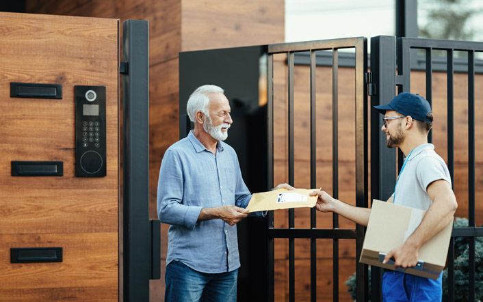 Delivery handoff at a modern house gate, with two people exchanging a package.