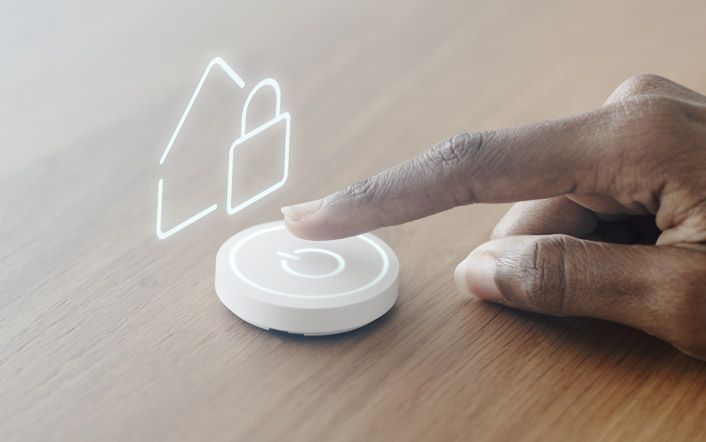 Finger pressing a smart home button beside a glowing lock icon on a wooden table