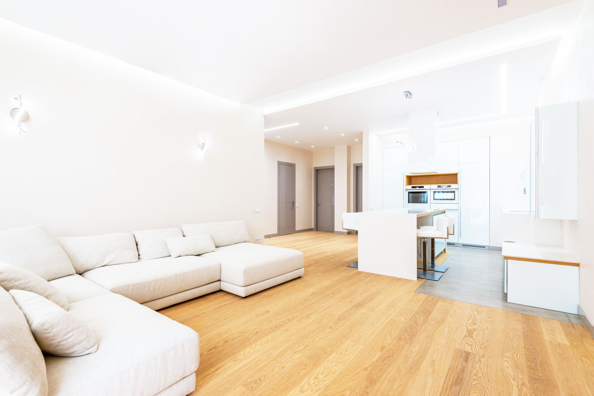 Bright modern living room with white sectional sofa, wood floors, and open kitchen area
