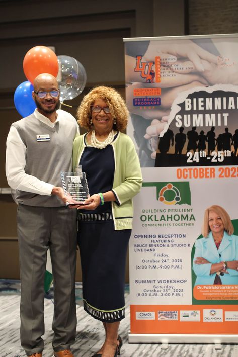 Man presenting an award to a woman at a conference. Poster in the background.