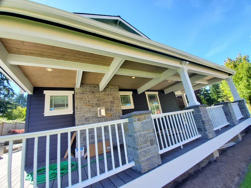 Dark blue house with white trim, porch with stone columns, white railing, and wooden ceiling.