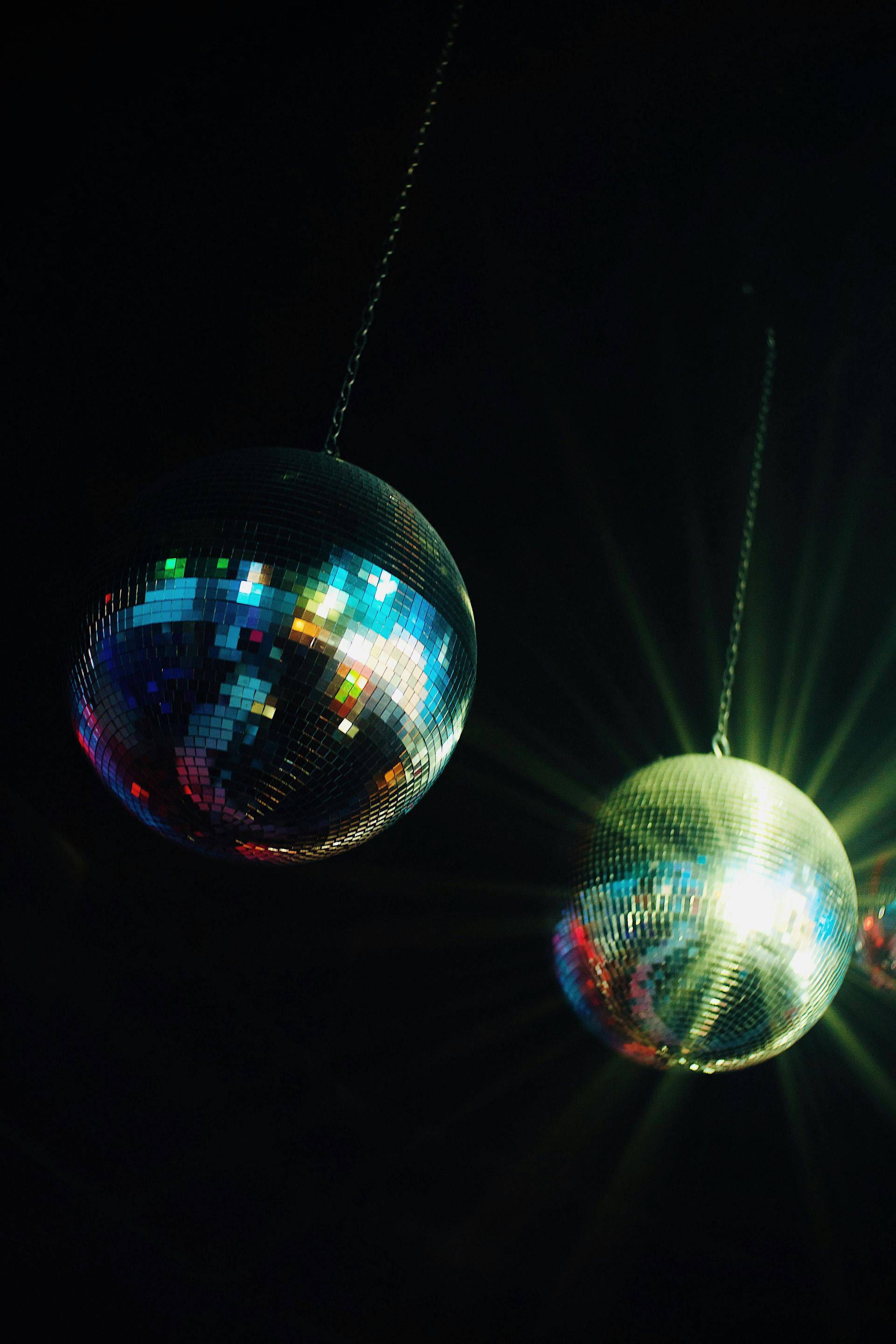 Two disco balls are hanging from a chain in the dark.