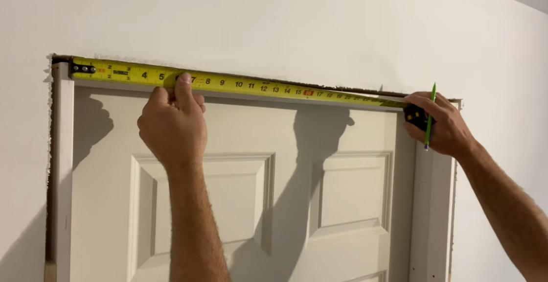 Person measures door frame with tape measure and marks with pencil.