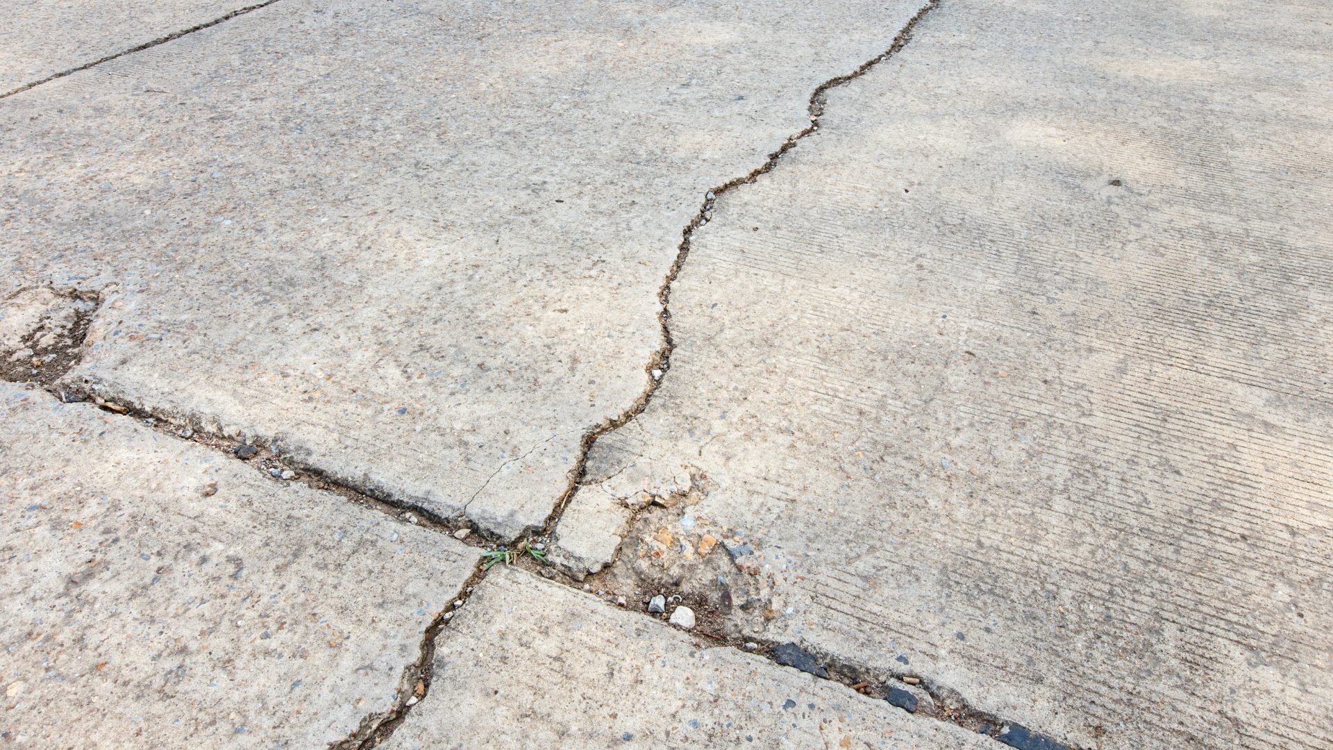 Cracked concrete pavement with a broken seam and small debris in the center