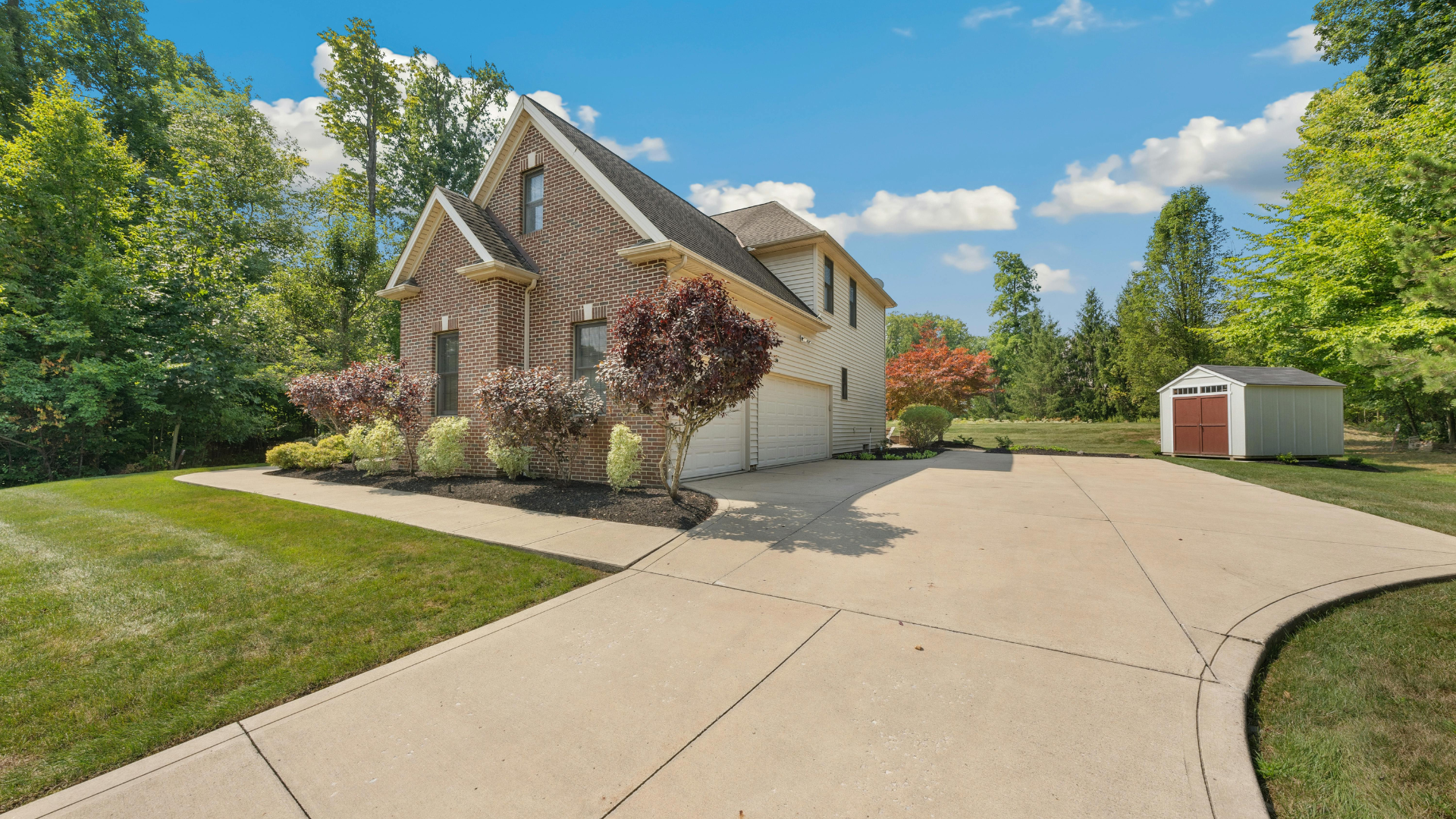 Suburban house with a curved driveway, landscaped yard, and a small shed under a blue sky