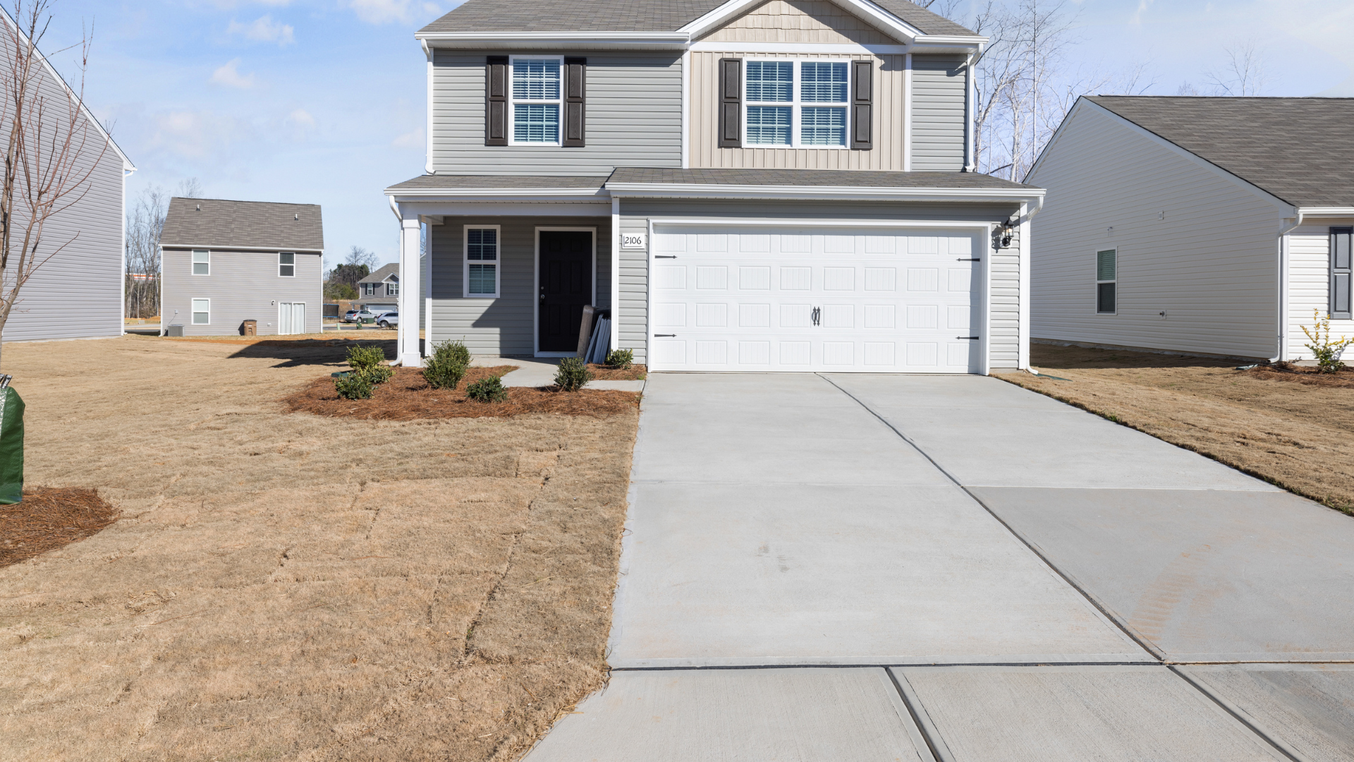 Two-story suburban house with white garage and long concrete driveway with expansion joints