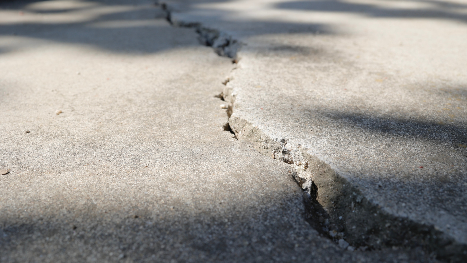 Cracked concrete pavement with a long fissure in sunlight and shadow
