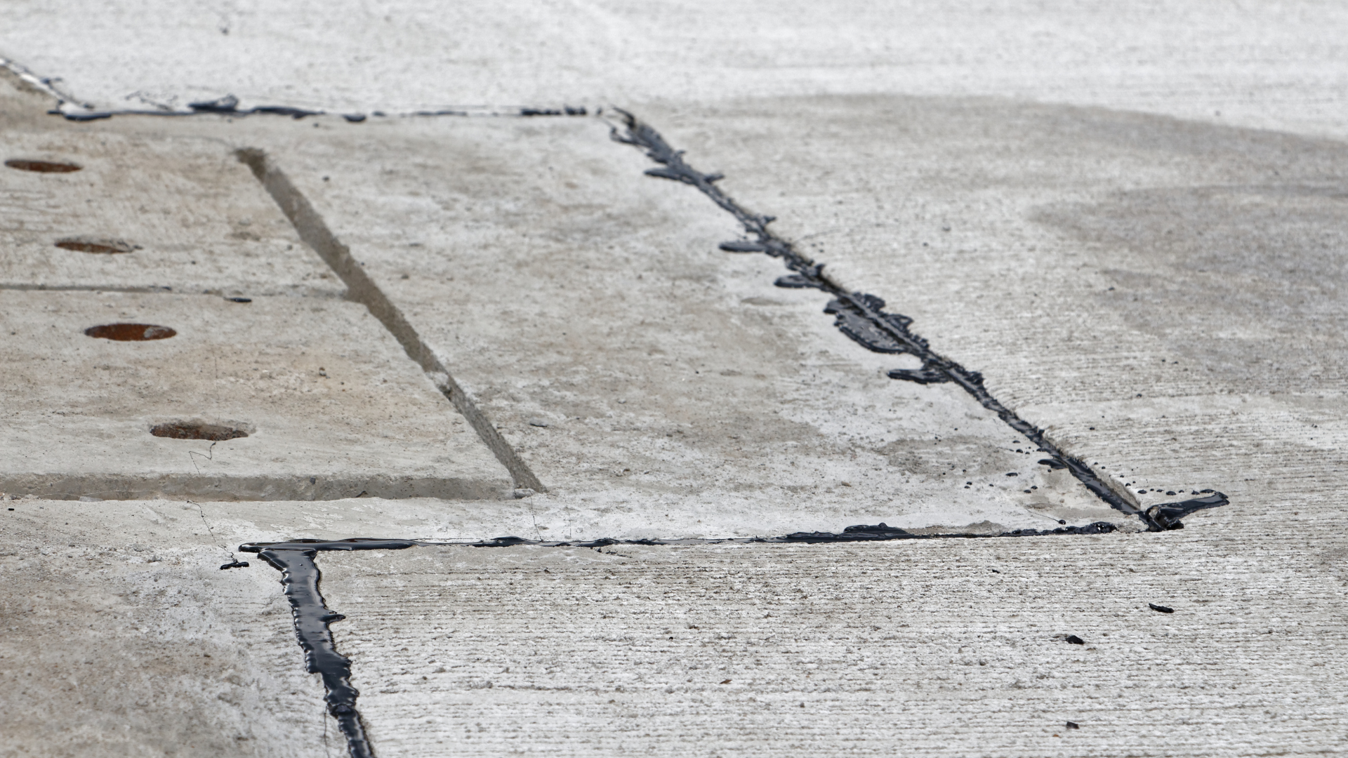 Cracked concrete pavement with repaired seams and holes along a sidewalk or roadway