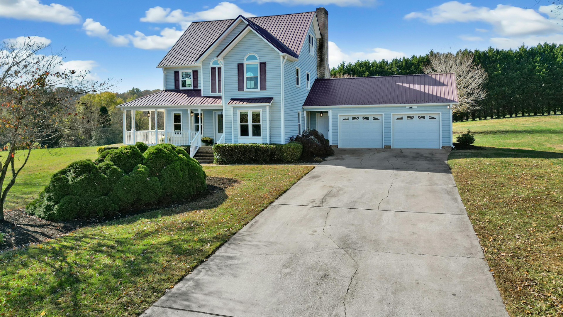 Two-story blue house with a front porch, double garage, and long concrete driveway on a grassy lot