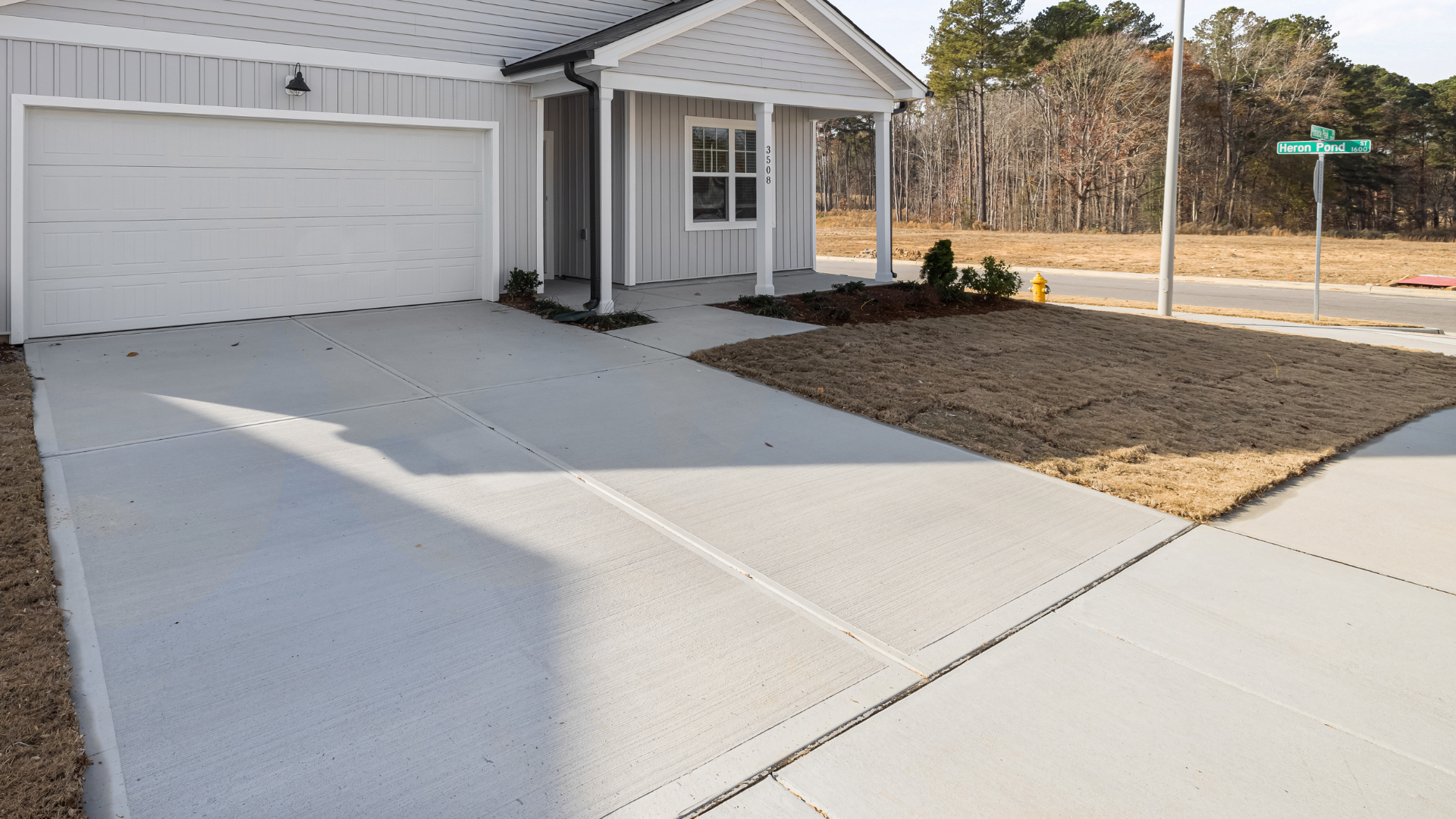 Single-story house with white garage, front porch, and a wide concrete driveway on a corner lot.