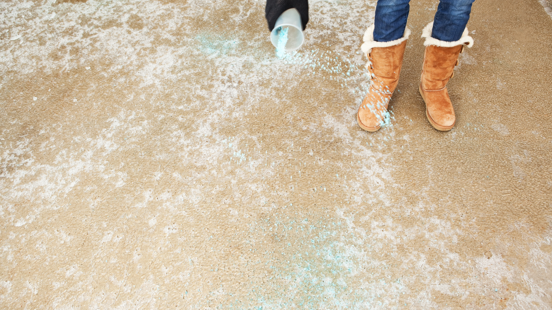 Person pouring deicing salt on concrete driveway to help melt snow