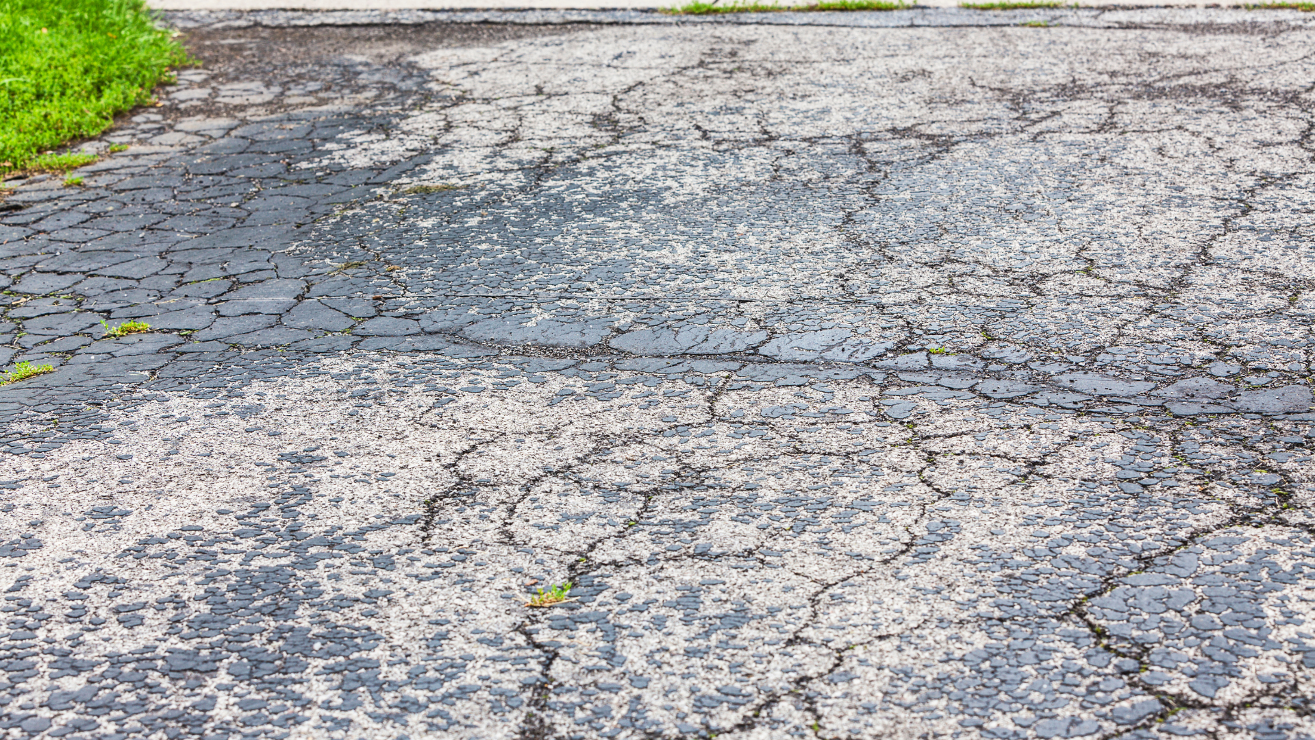 Cracked asphalt road with patches of grass along the edge