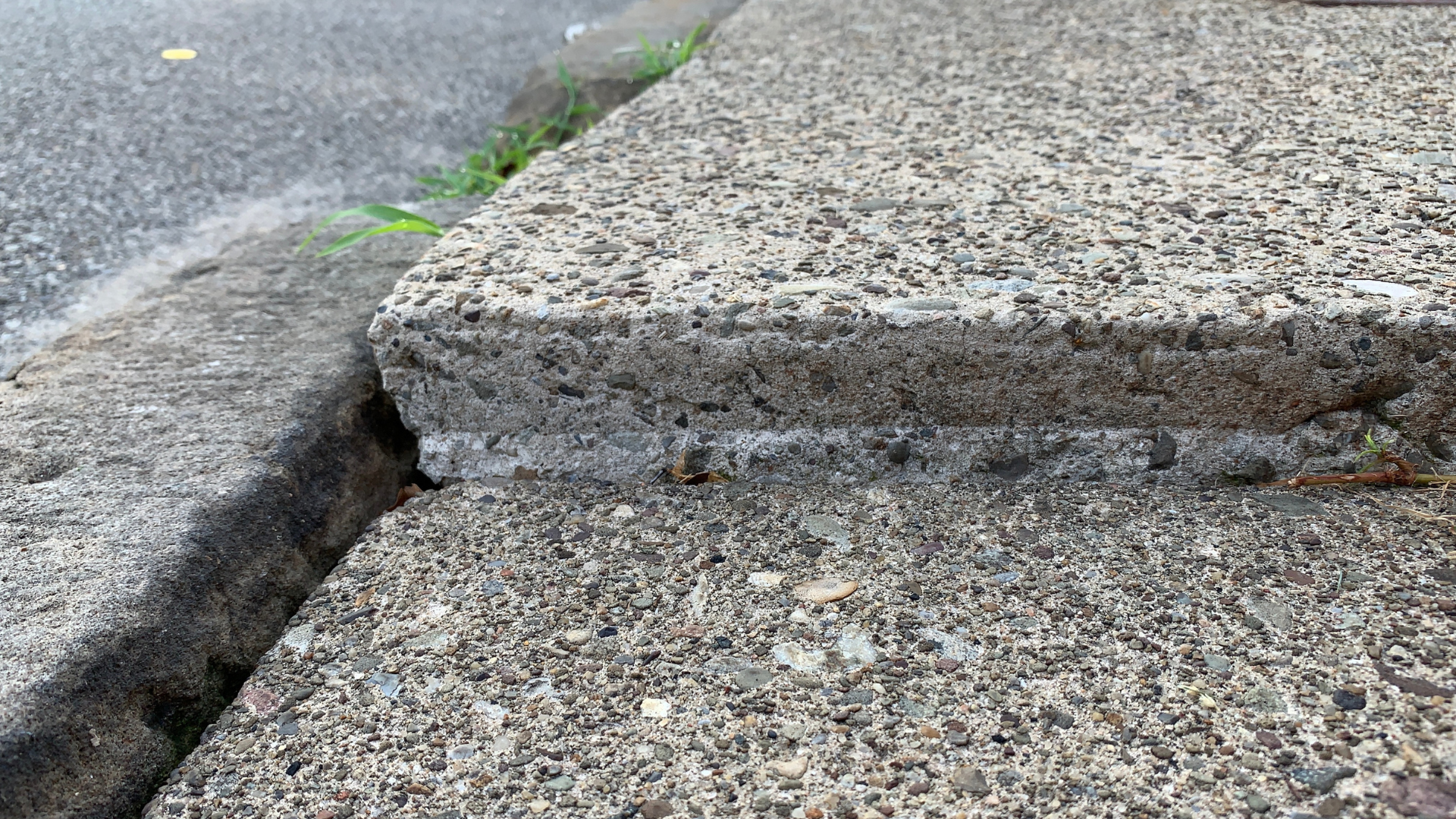 Cracked curb and broken concrete sidewalk with a gap between slabs
