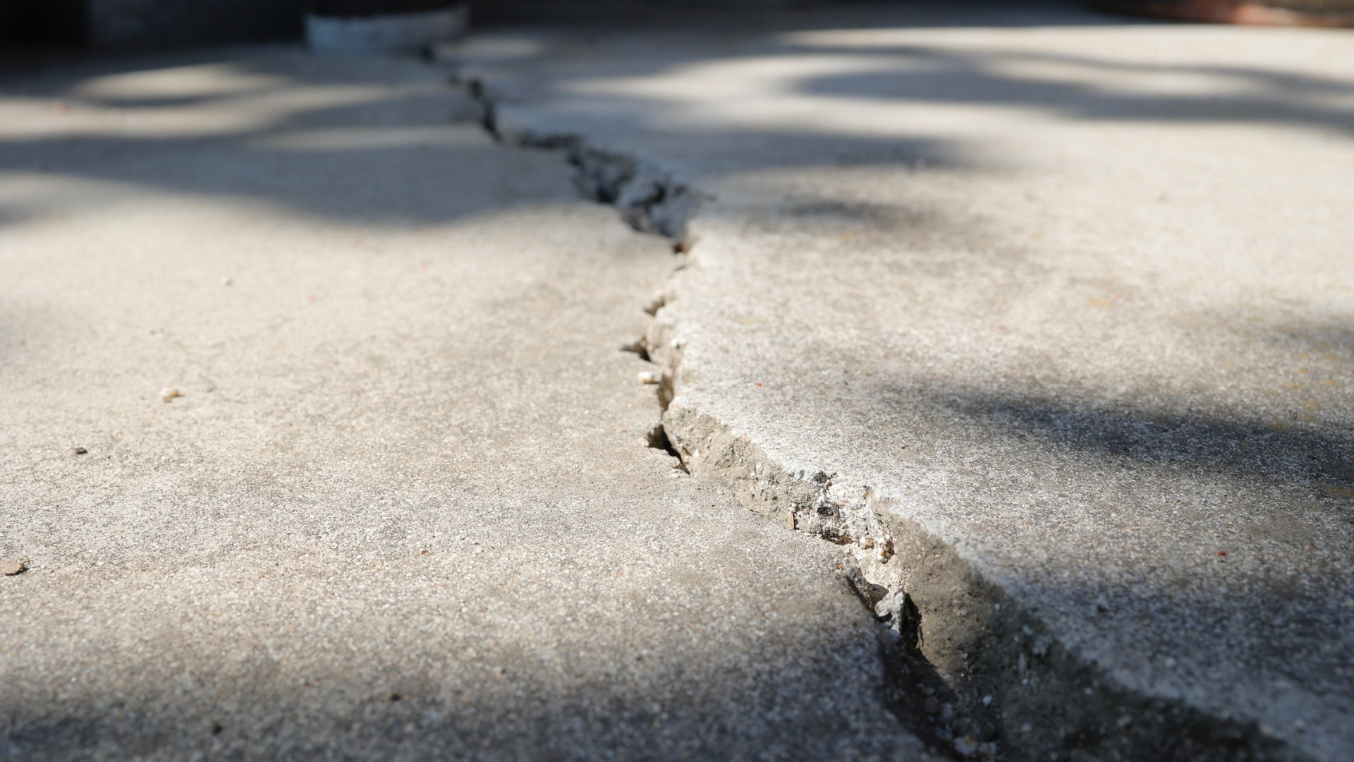 Cracked concrete pavement with a jagged split running through it in sunlight and shadow.