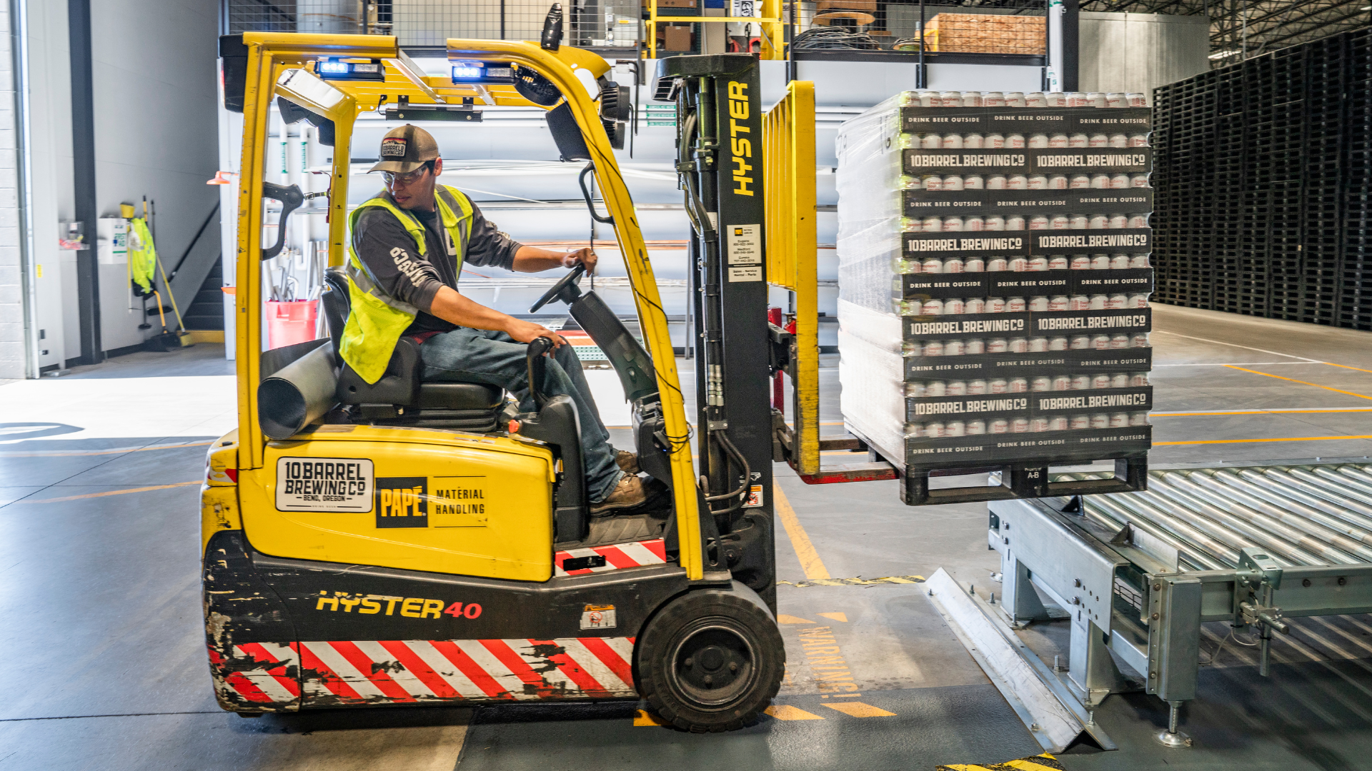 Yellow Hyster forklift carrying stacked trays in a warehouse aisle
