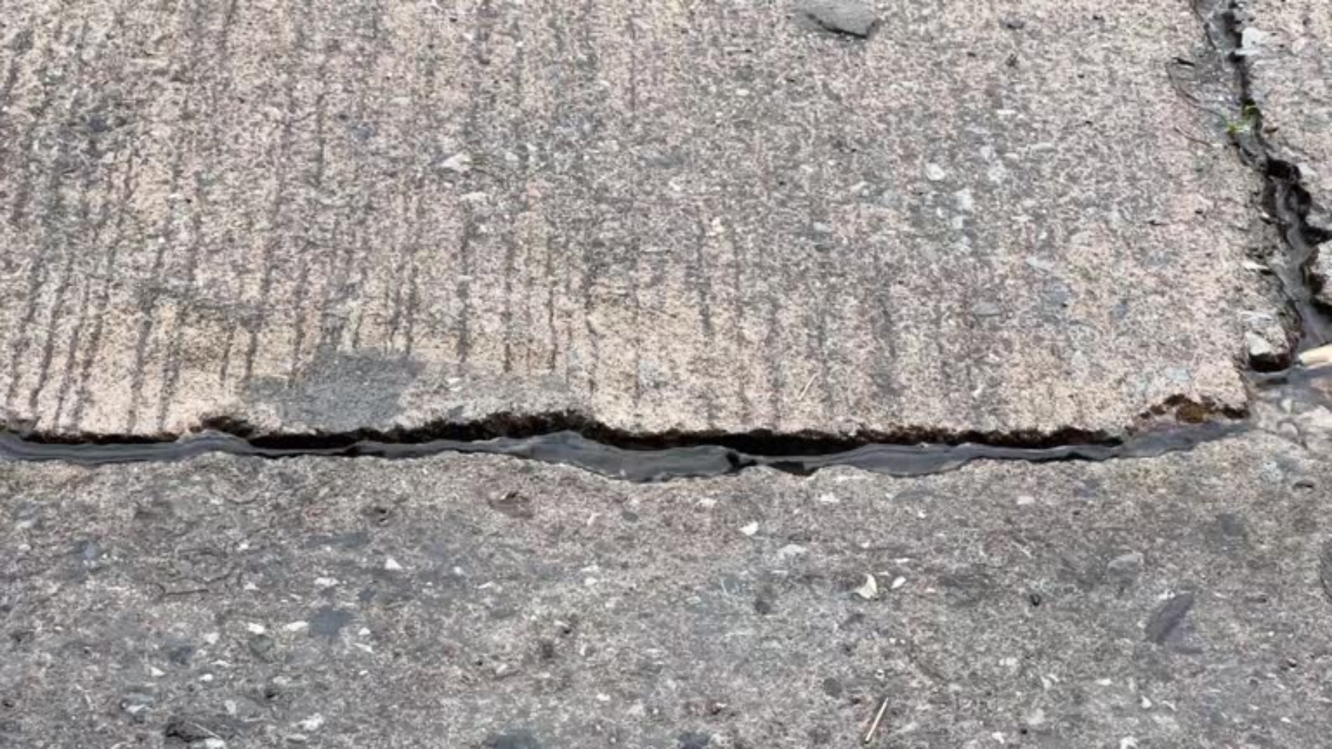 Close-up of cracked, weathered pavement with a raised edge