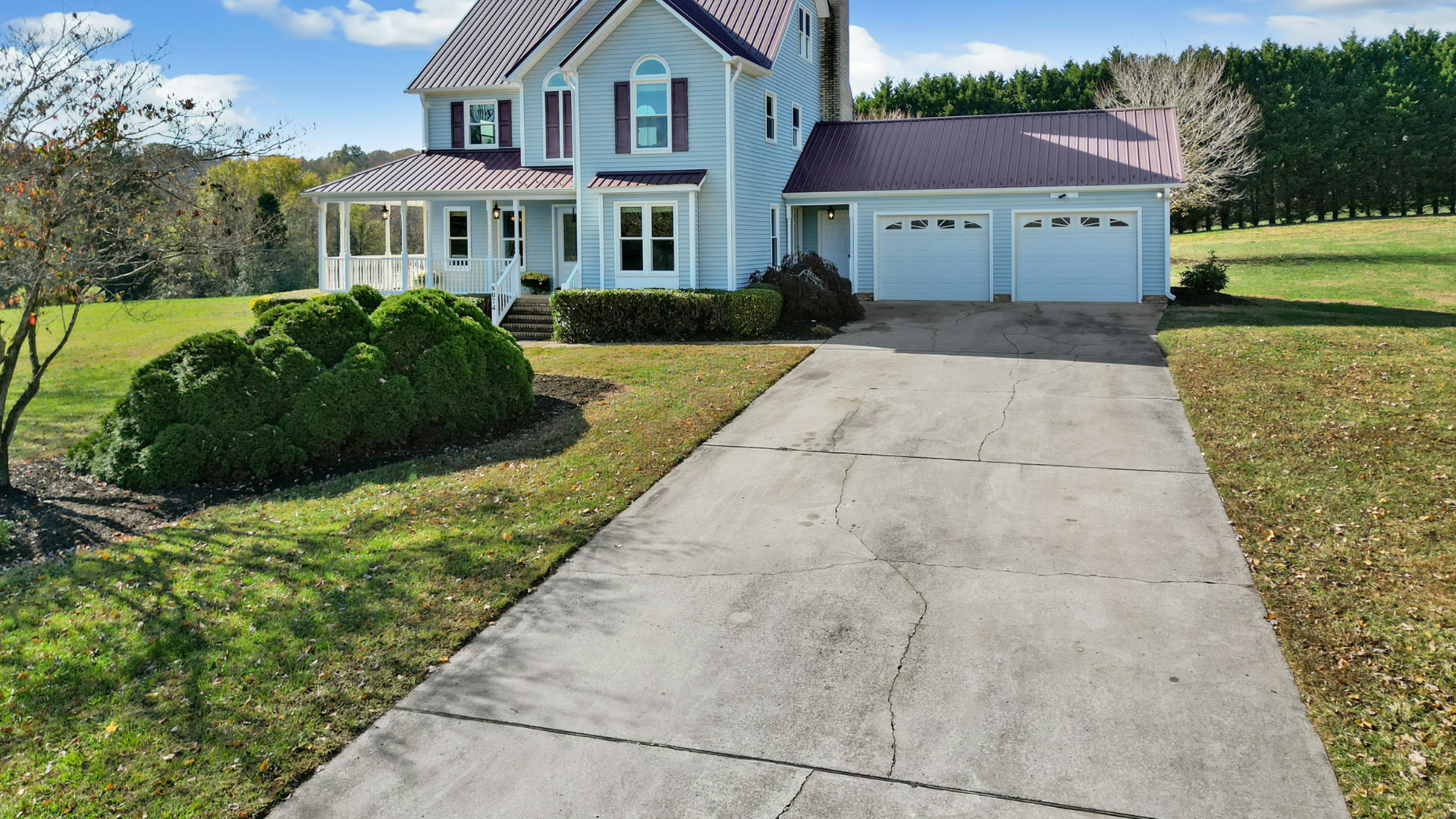 Two-story light blue house with a two-car garage and long driveway on a sunny suburban lot