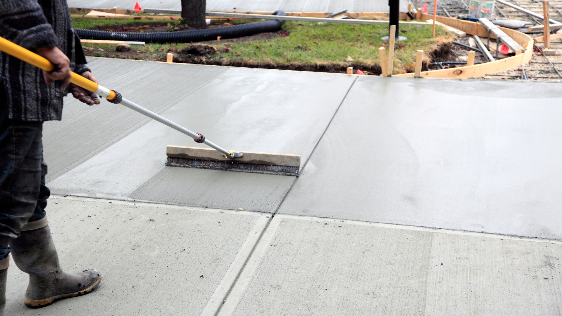 Worker smoothing fresh concrete with a long-handled float on a sidewalk
