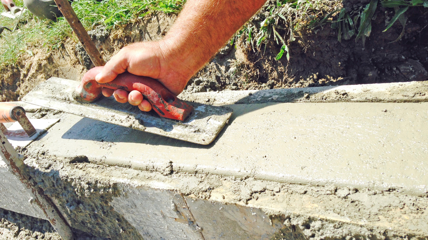 A person uses a hand trowel to smooth wet cement on a construction form outdoors.