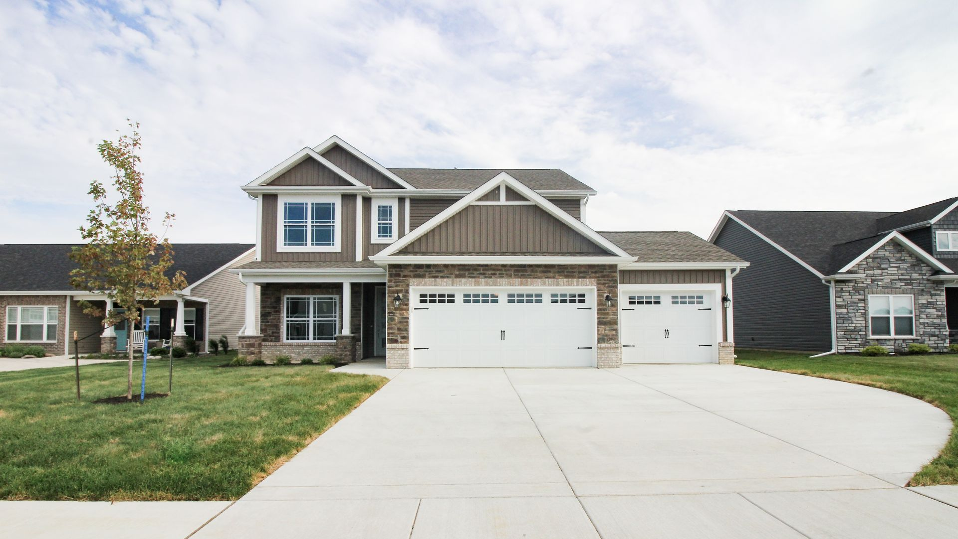 A two-story suburban house with brown vertical siding, a stone facade, and a three-car garage, set under a cloudy sky.