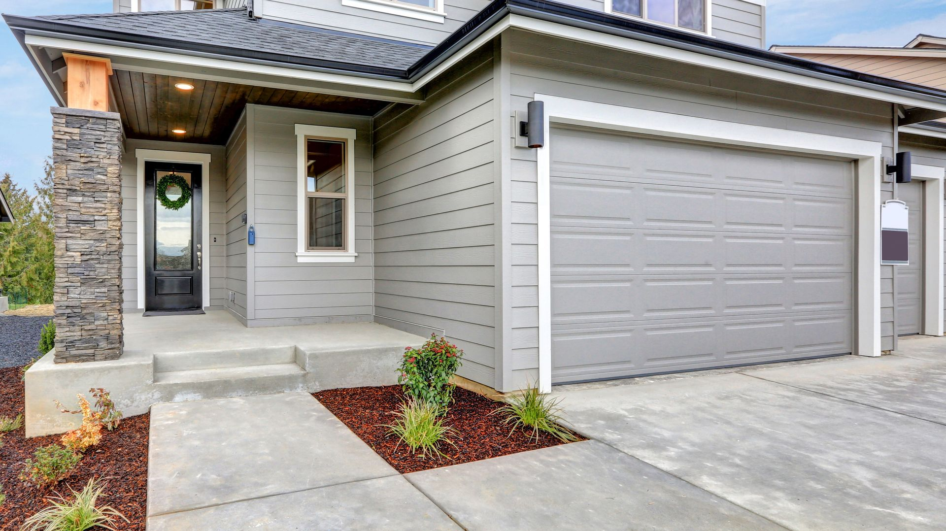 Modern house exterior with gray siding, front porch, and two-car garage driveway