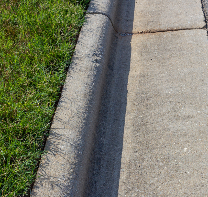 Concrete curb separating green grass from a concrete sidewalk.
