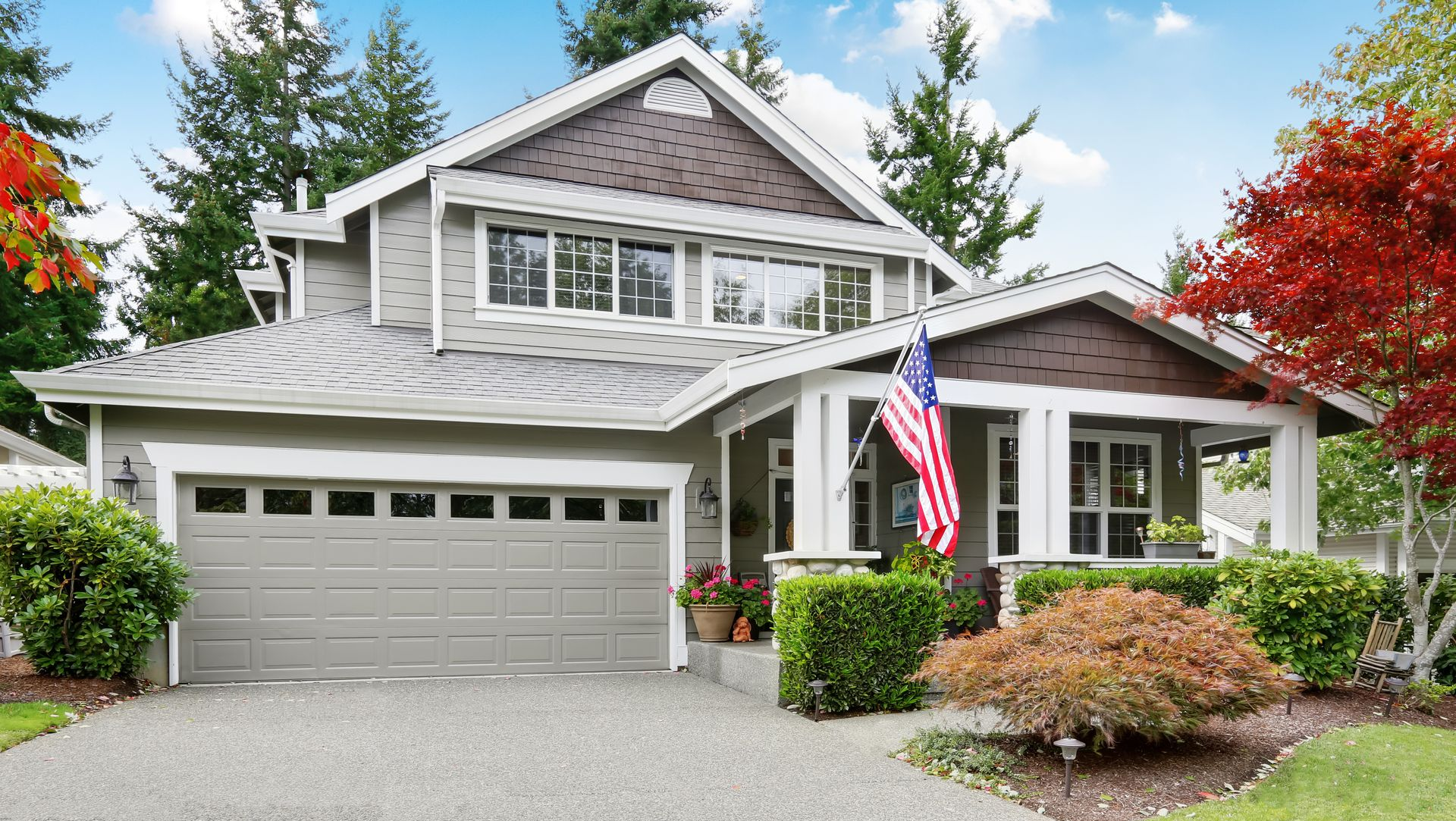 Gray suburban house with two-car garage, American flag, and manicured front yard in spring