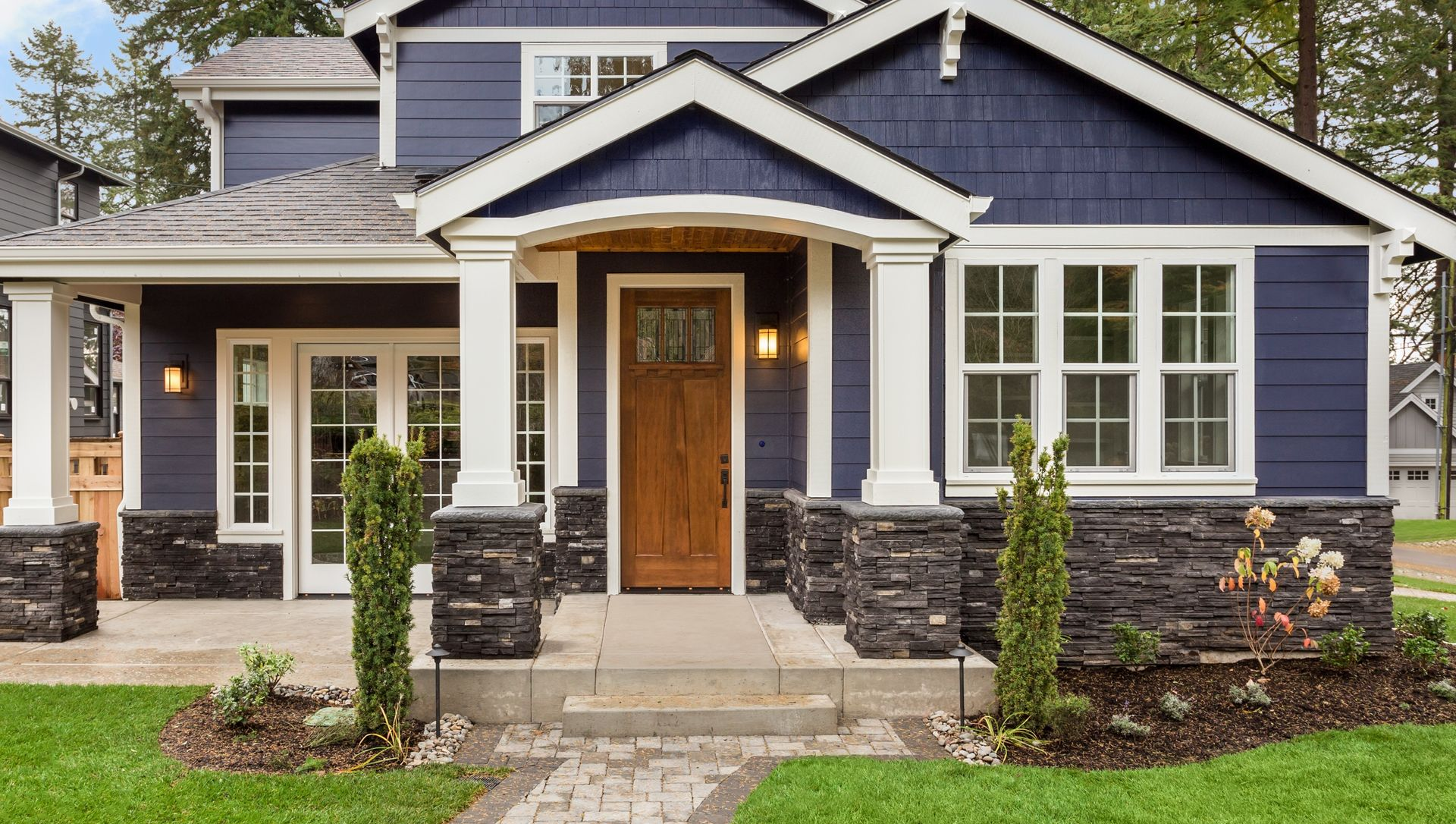 Blue house with stone porch, wooden front door, and curved brick walkway surrounded by green lawn.