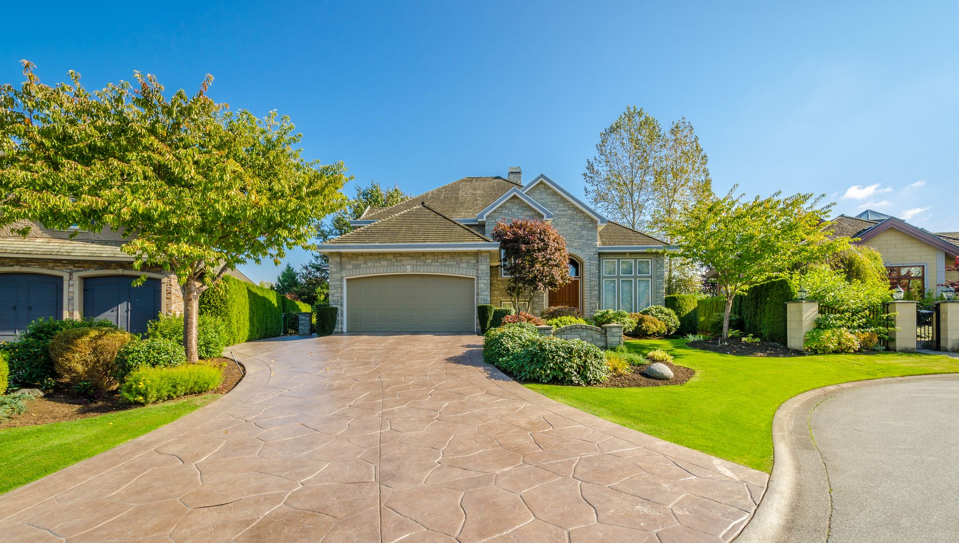House with brown stamped concrete driveway and manicured lawn under a blue sky.