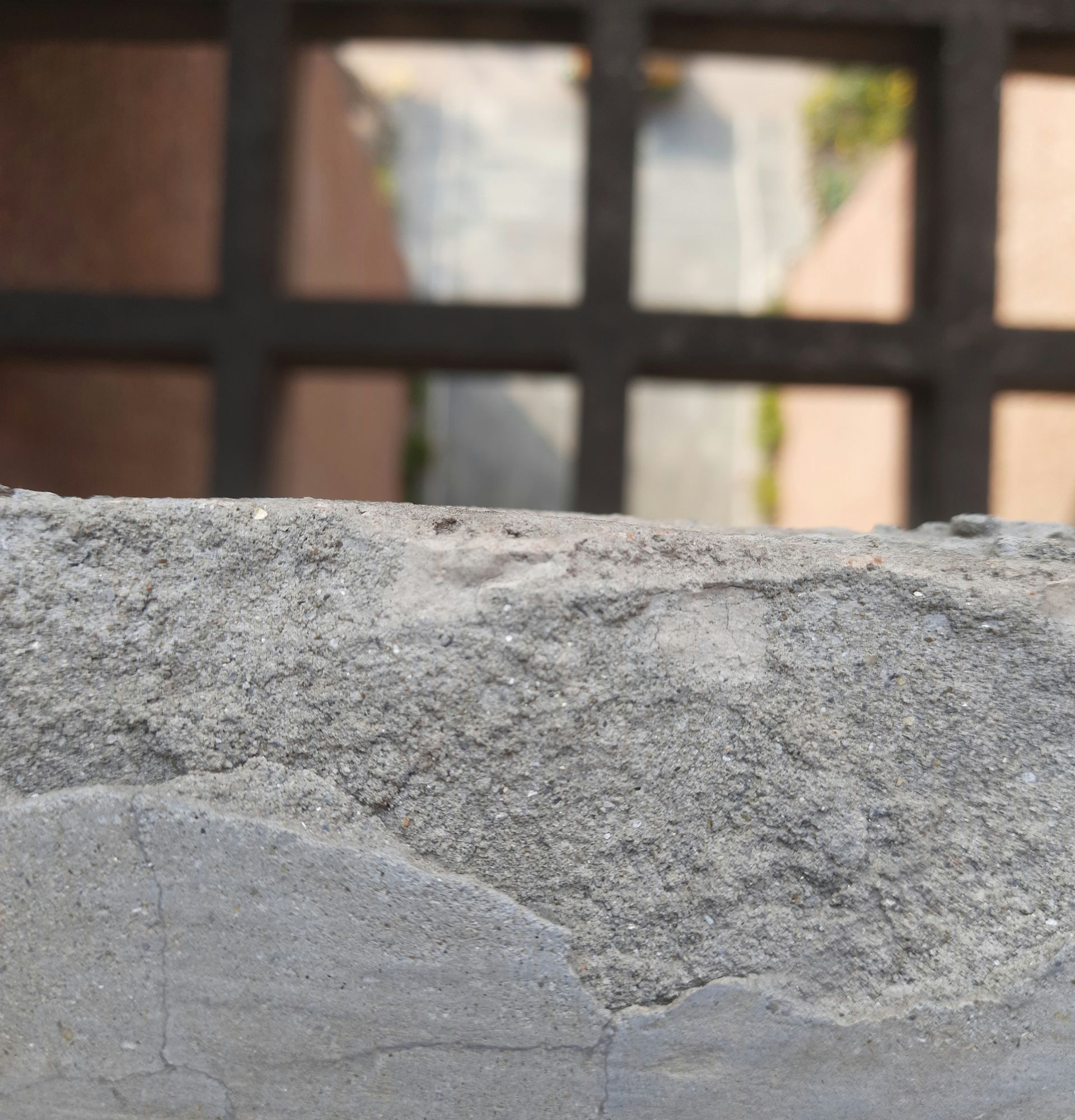 Gray concrete wall with a blurred window and black metal bars in the background