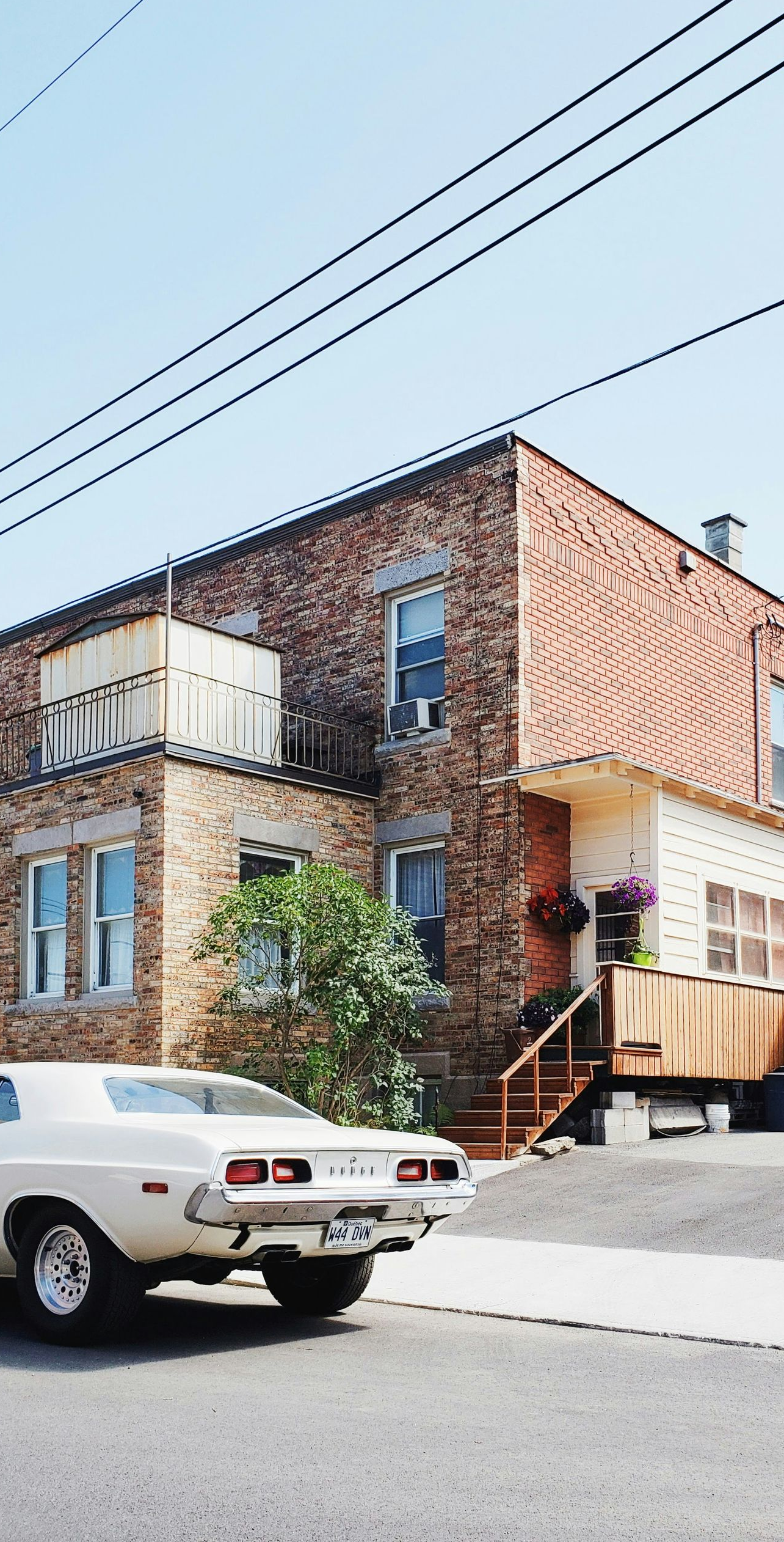 Brick building on a sloped street with a white car parked in front and overhead power lines.