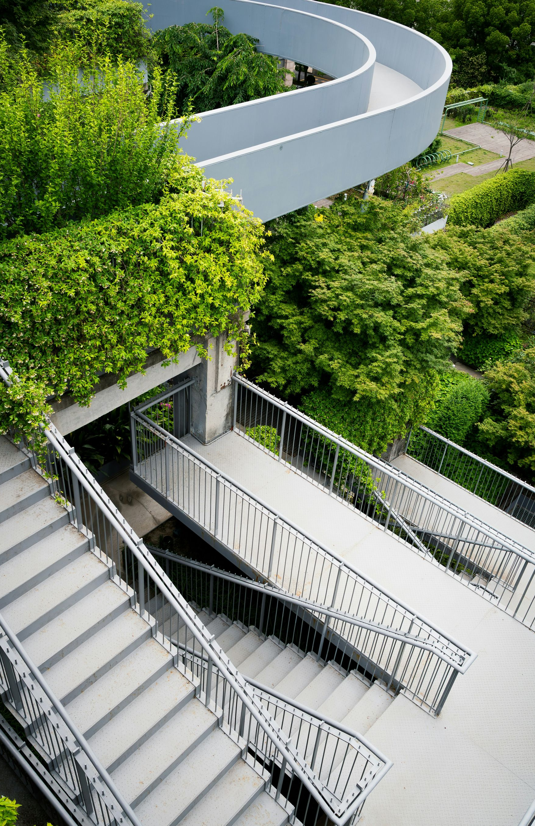 White curved stairway beside a lush green rooftop garden and concrete ramp