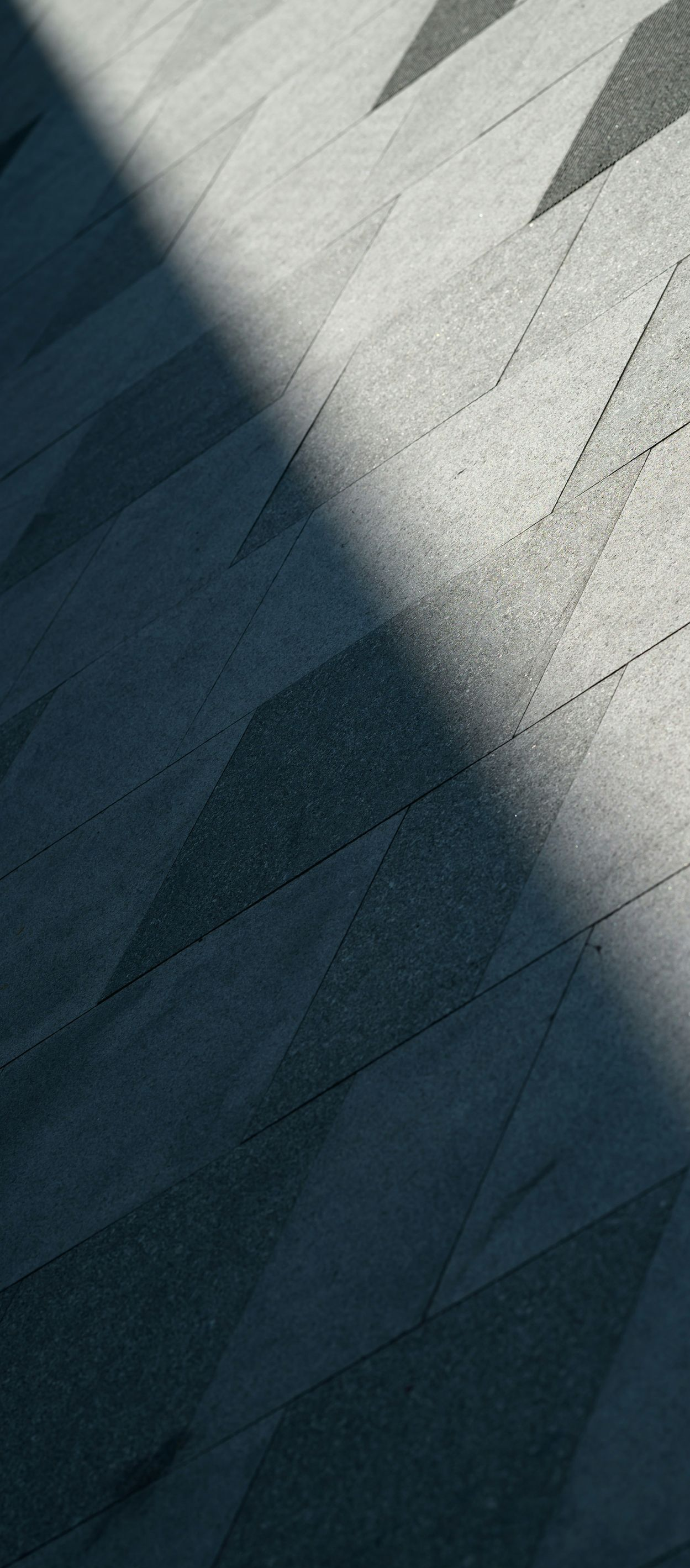 Abstract geometric pattern of light and dark triangular shadows on a textured gray surface