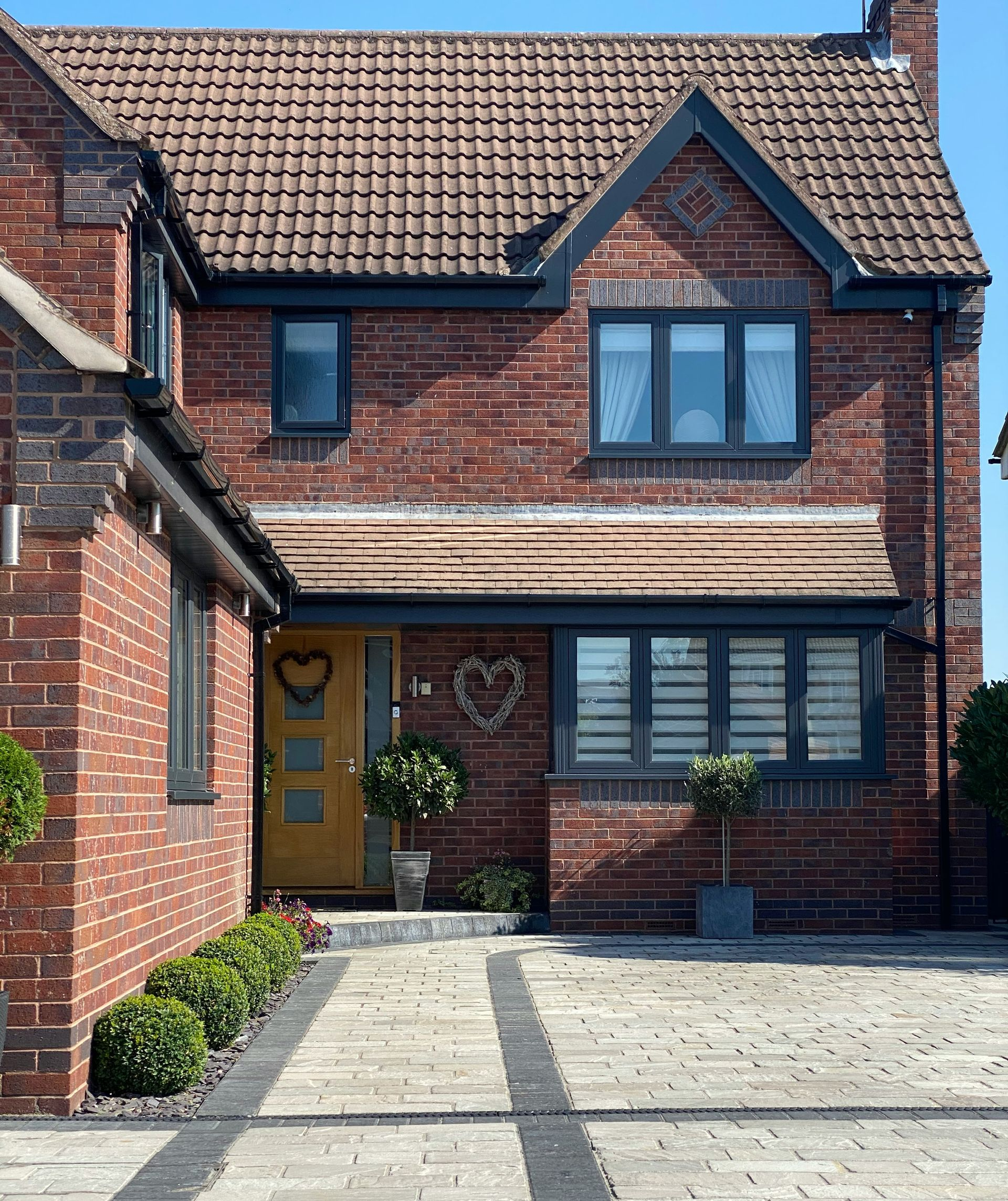 Brick house with gray window frames and a yellow door, a paved driveway, and small garden.