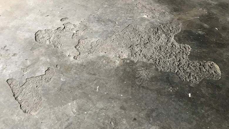 Cracked, peeling concrete floor with rough patches and worn gray surface