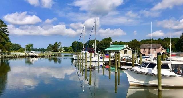 Boats docked at a marina with reflections on the water under a blue sky with clouds.
