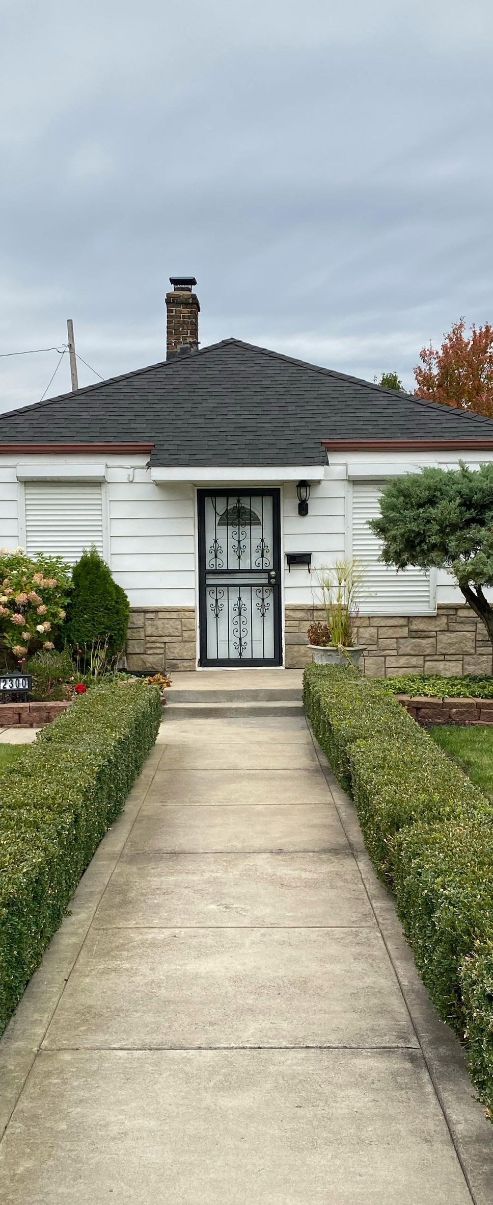 Front view of a small white house with a concrete walkway and garden beds leading to the front door