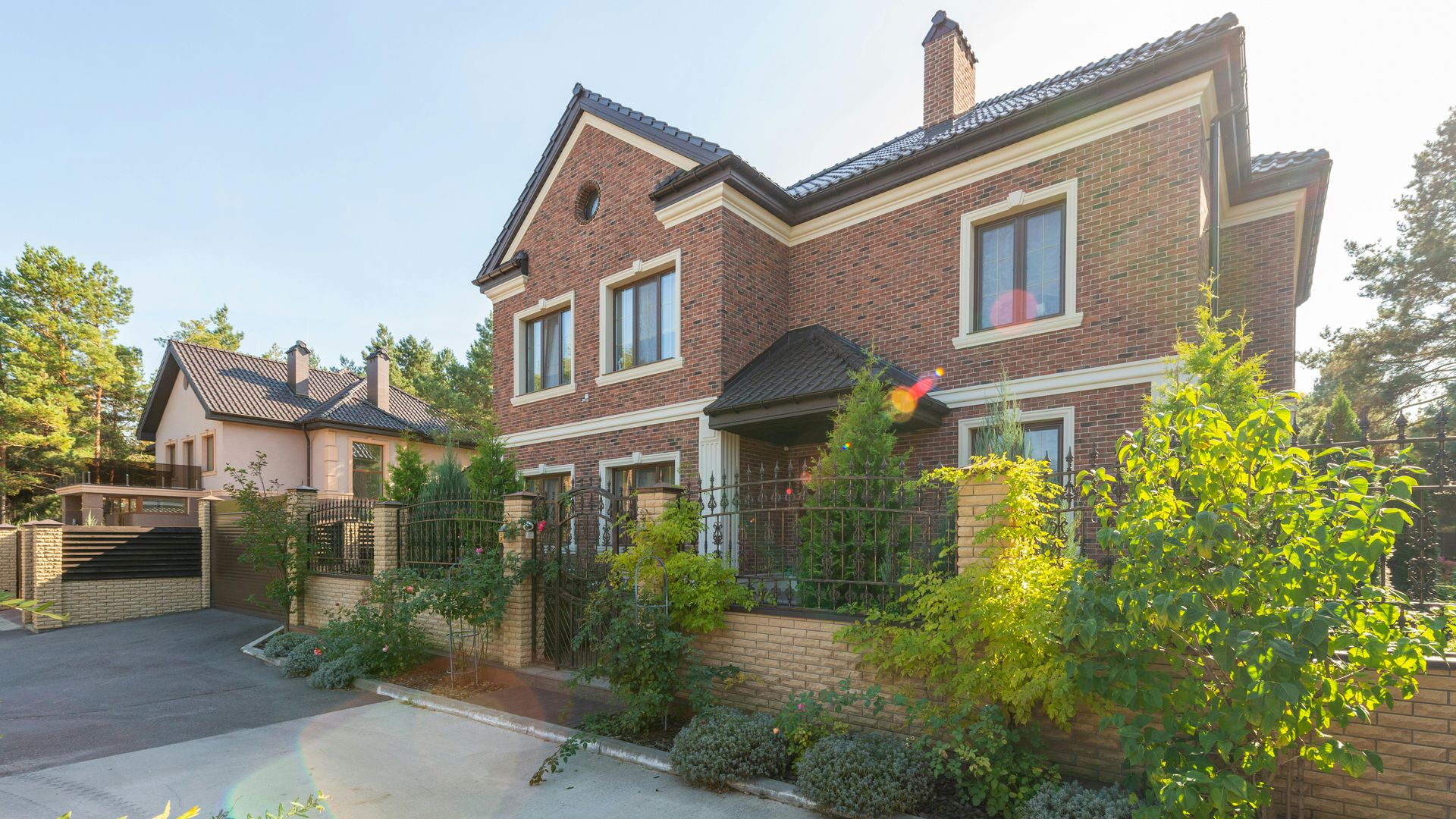 Brick two-story house with a front garden, driveway, and sunlit suburban street