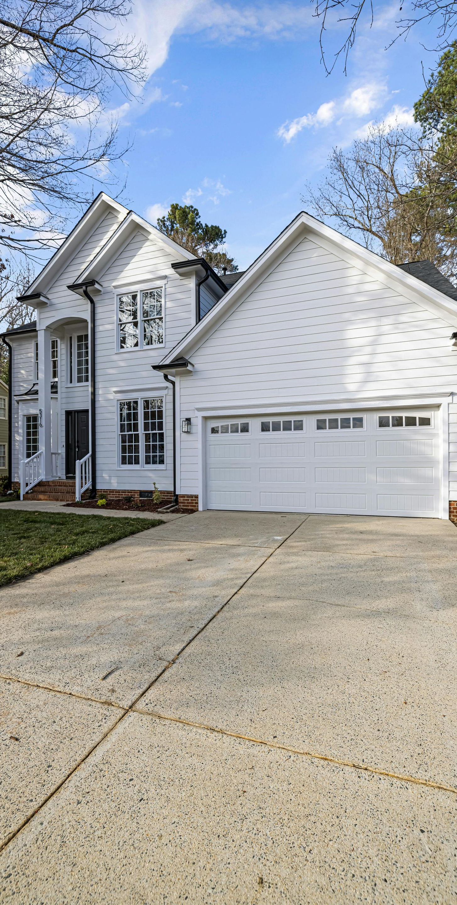 White two-story house with attached two-car garage and concrete driveway under a blue sky