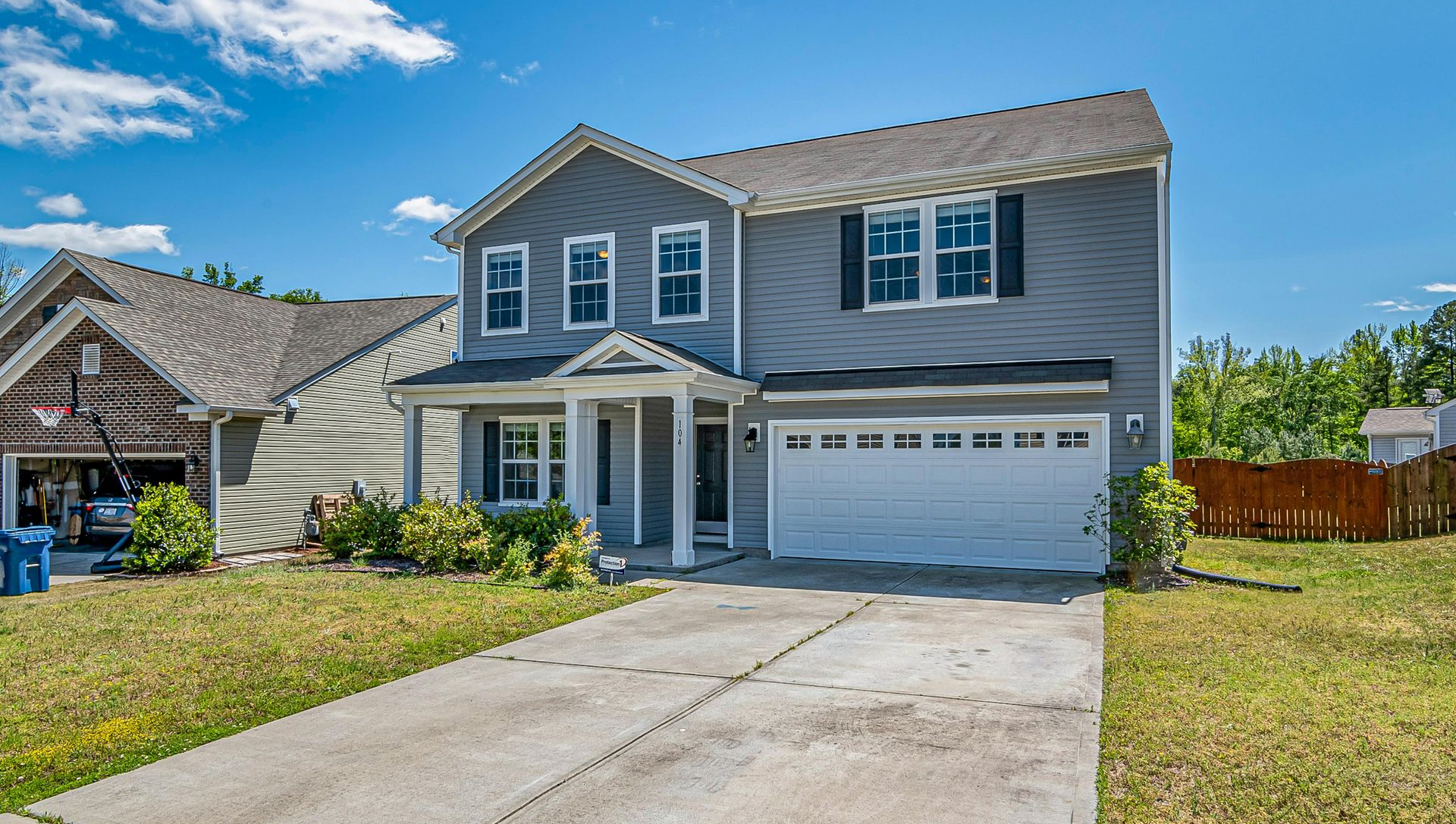 Suburban two-story gray house with white trim, garage, and a concrete driveway under a blue sky