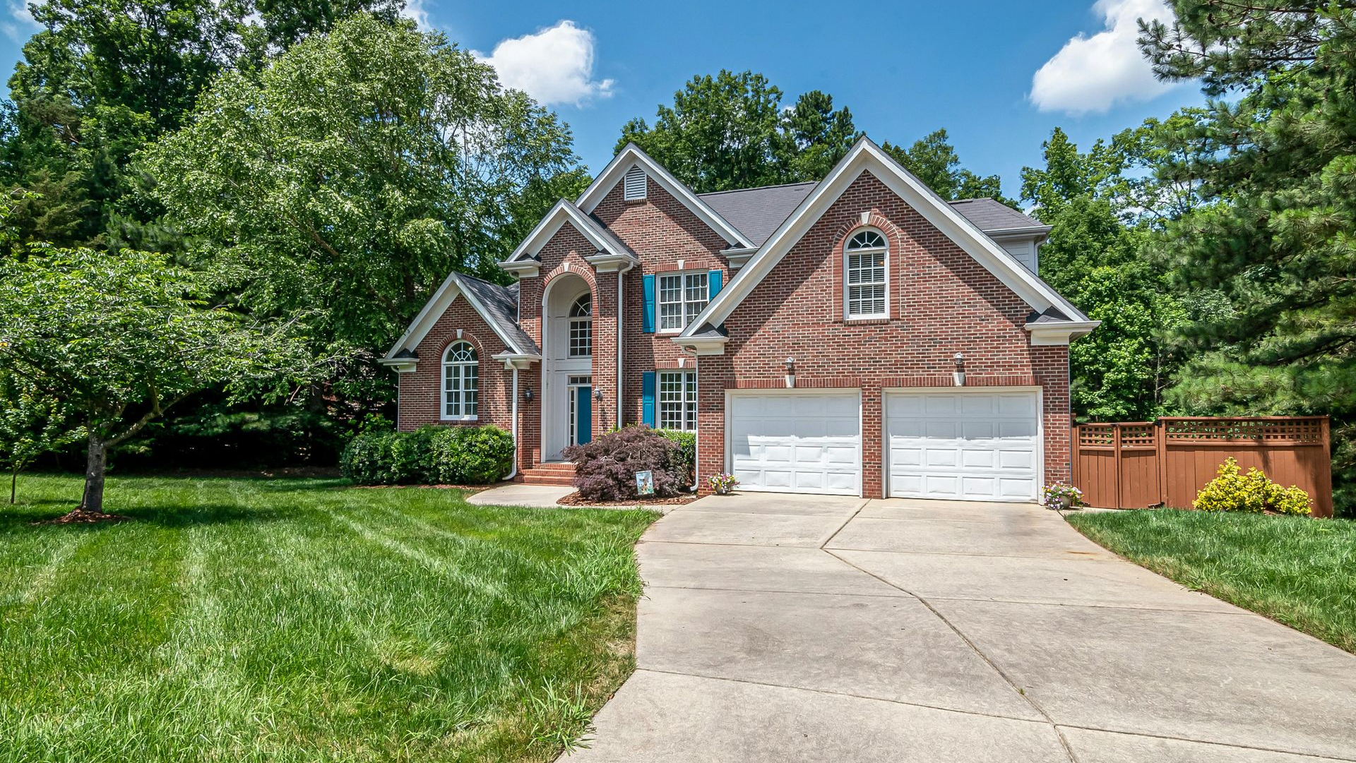Suburban brick house with two-car garage, curved driveway, and green lawn on a sunny day