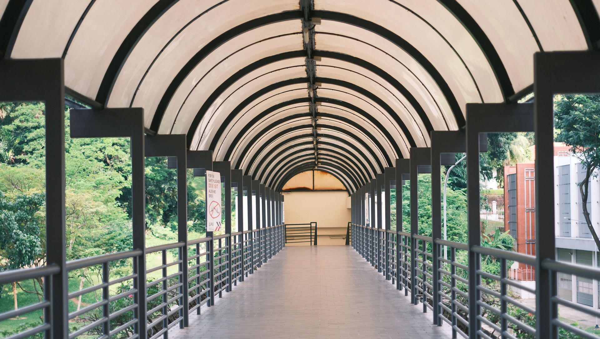 Covered pedestrian walkway with arched roof, railings, and greenery on both sides