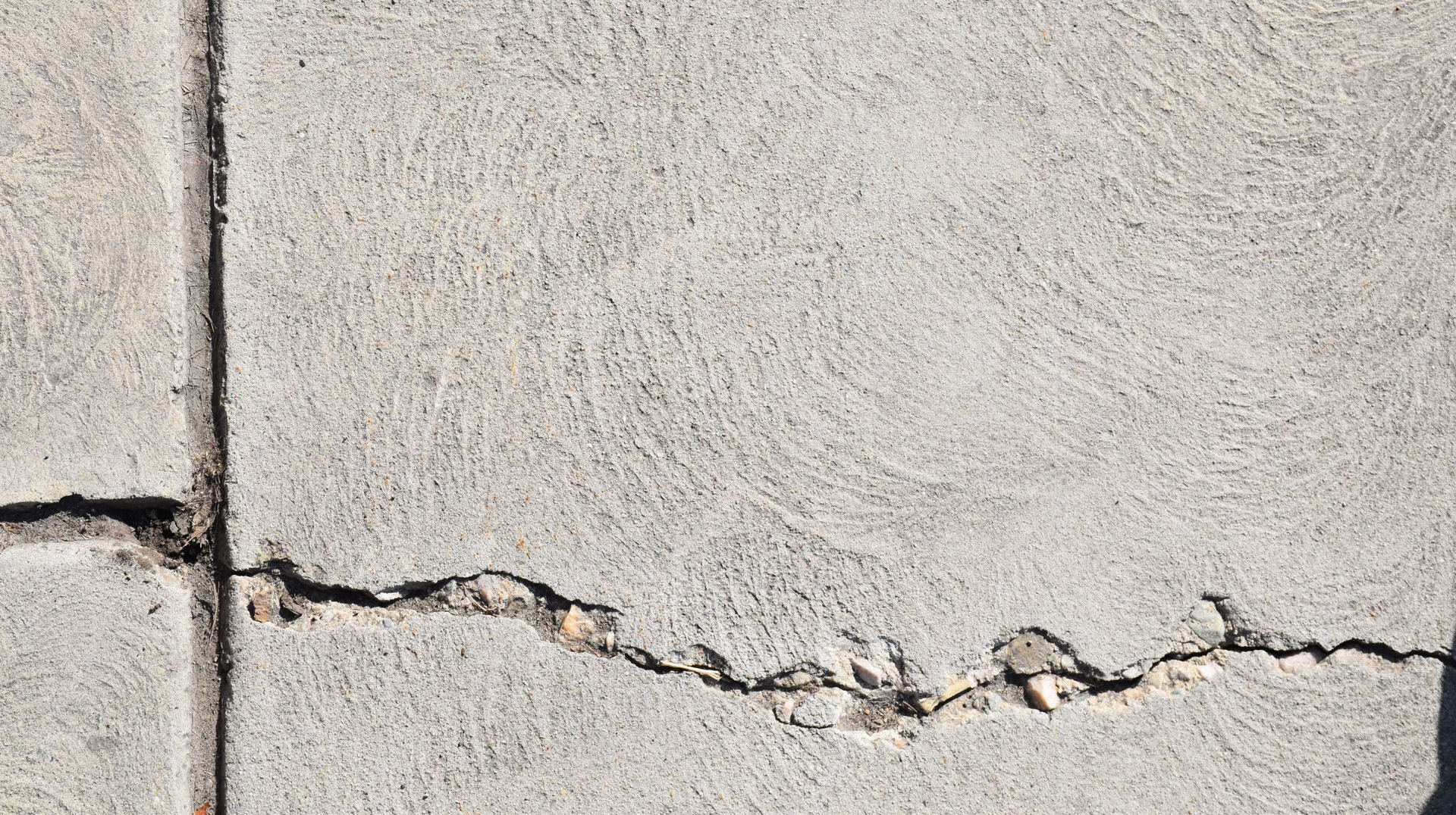 Cracked beige concrete wall with a horizontal fracture near the bottom left